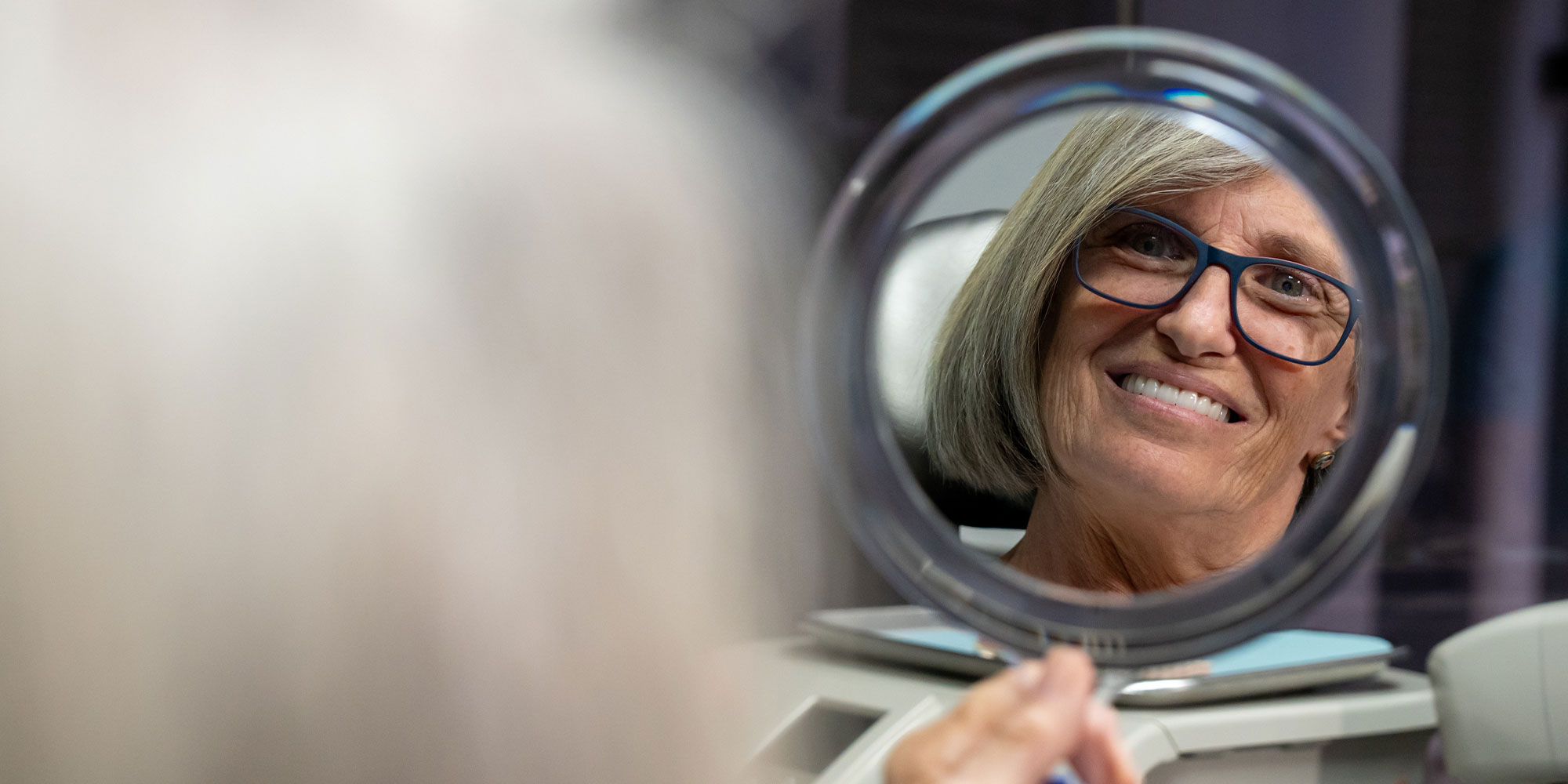 patient smiling brightly within a handheld mirror after their dental treatment
